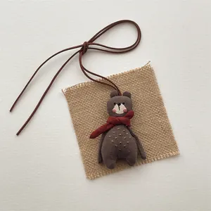 Detailed view of a handmade brown linen plush bear pendant with a red scarf and yellow embroidery