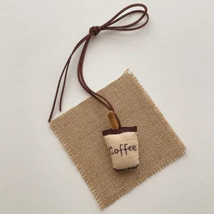 Detailed view of a mini fabric coffee cup plush charm with embroidery and brown lanyard