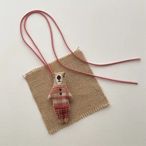Detailed view of handmade fabric bear pendant with red check shirt and leather strap