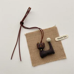 Close-up of a handmade polka dot plush cat pendant with golden bell on burlap texture