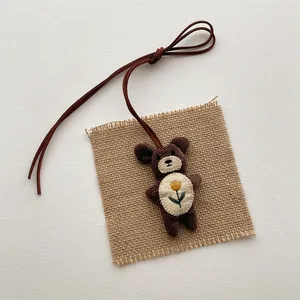 Detail of a brown corduroy plush bear pendant with embroidered flower and long lanyard