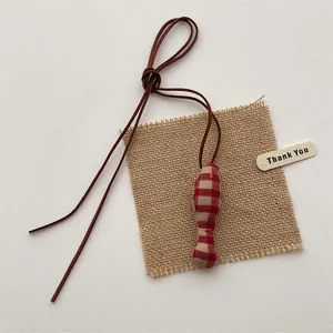 Detail of a handmade red-brown plaid fabric fish pendant with a long brown cord