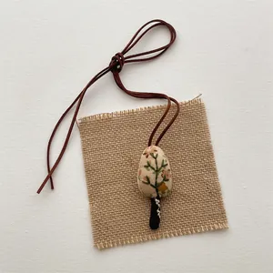 Close-up of handmade fabric necklace featuring delicate tree embroidery on canvas