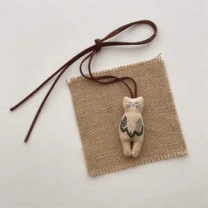 Detail of handmade embroidered cat fabric pendant with floral pattern and suede lanyard