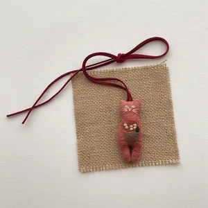 Detailed view of a handmade pink fabric cat charm with embroidery and a red velvet cord