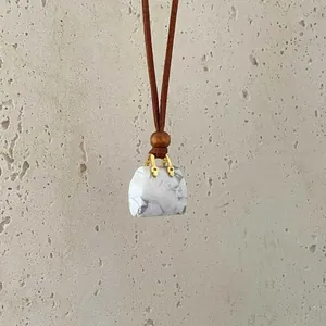 Detail of miniature marble stone bag pendant with gold hardware on a brown leather cord