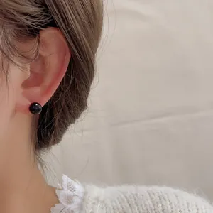 Nahaufnahme minimalistischer schwarzer Onyx-Ohrstecker kombiniert mit weißem Spitzenpulli