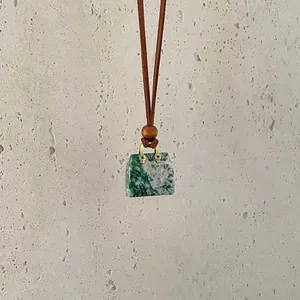 Detail of a natural green agate handbag pendant with gold handle on a brown cord