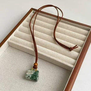 Macro detail of natural stone pendant with gold clasp and leather rope on a linen tray