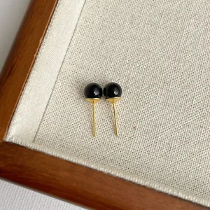 Detaillierte Nahaufnahme eleganter schwarzer Achat-Ohrstecker mit Vergoldung auf Stoff