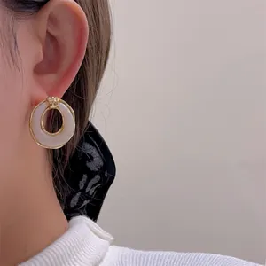Nahaufnahme eleganter goldgerandeter weißer Harzohrstecker an einem Model bei sanftem Licht