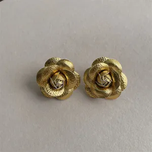 Macro detail of golden camellia flower stud earrings with layered metallic petals