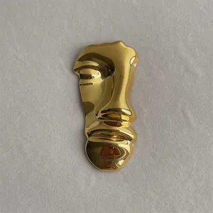 Detailed view of an abstract golden face brooch with a high-shine mirror finish on grey fabric