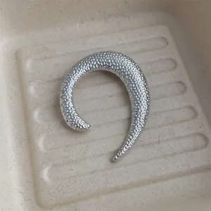 Dettaglio ravvicinato della spilla a U irregolare color argento con finitura in metallo martellato