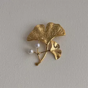 Détail de la broche feuille de ginkgo dorée avec textures fines et deux perles blanches