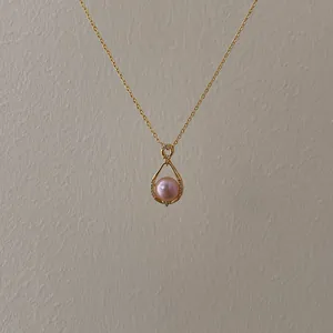 Macro shot of a pink pearl pendant in a gold-plated teardrop frame with diamonds