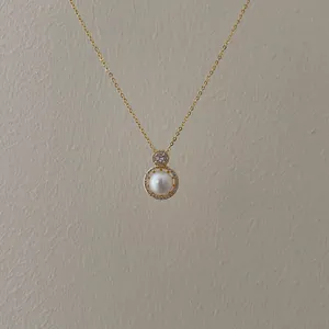 Close-up of golden necklace featuring a white pearl pendant within a sparkling crystal ring