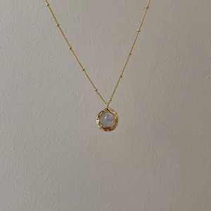 Detail of a gold satellite chain necklace with a hammer-textured shell pendant