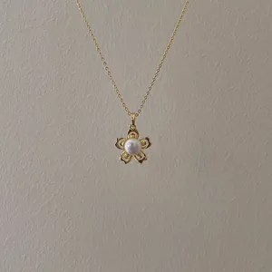 Detail of a minimalist gold flower pendant with a central freshwater pearl on a thin chain