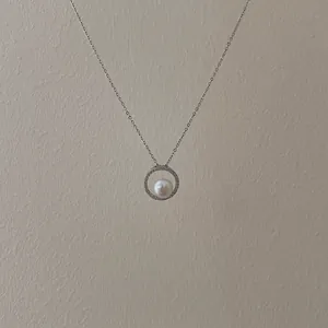 Detail of silver chain necklace with a diamond-encrusted circular pendant and white pearl