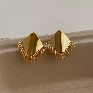 Close-up of golden geometric stud earrings with layered metallic chain fringe tassels