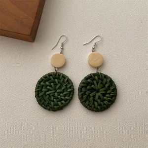 Close-up of bohemian green woven rattan earrings with small wooden disc and metal hook
