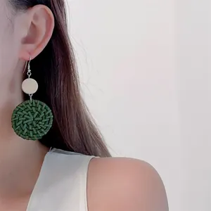 Detail of hand-woven dark green rattan disc earrings on a model with bohemian style