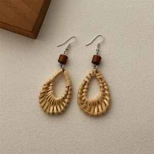 Macro detail of bohemian woven rattan teardrop earrings with a brown wood bead and metal hook