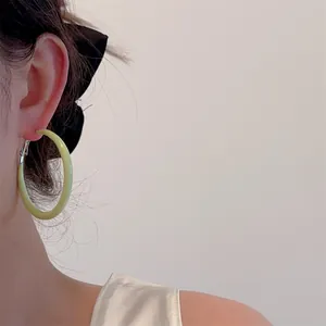 Close-up of light green oversized hoop earring with polished finish and metal clasp on ear