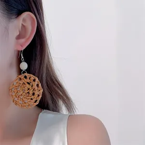 Detail of handmade woven rattan drop earrings with white bead on a model's ear