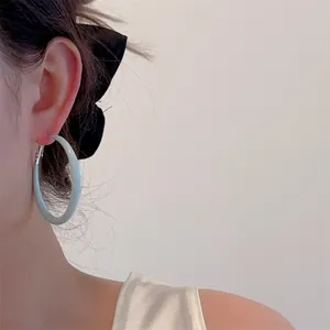 Close-up of matte light blue hoop earrings on model with elegant satin shirt