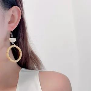 Close-up of bohemian style woven bamboo ring earrings worn by a model on white background