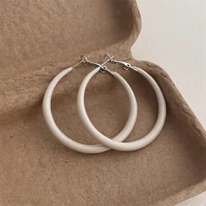Detailed close-up of cream-colored minimalist round hoop earrings in a brown gift box