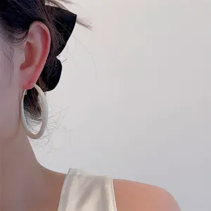 Close-up of model wearing large cream enamel hoop earrings with a minimalist glossy finish