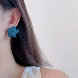 Close-up of a glossy deep blue star-shaped stud earring worn on a female earlobe