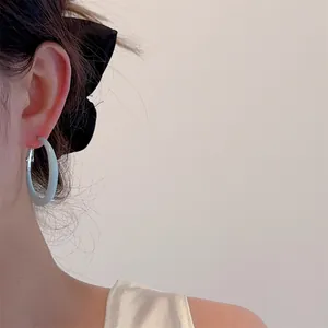 Close-up of light blue lacquer hoop earring worn by a model with a black bow hair tie
