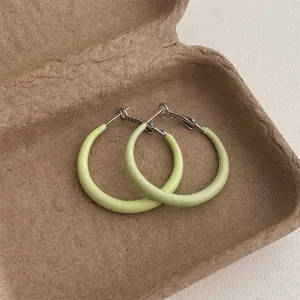 Close-up of light green matte finish hoop earrings on a textured paper tray