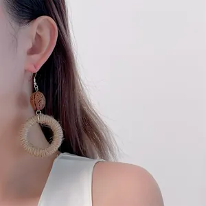 Detail of bohemian hand-woven straw hoop earrings with natural brown wooden beads