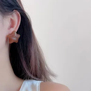 Detail view of a caramel star earring worn by a model with a glossy polished finish