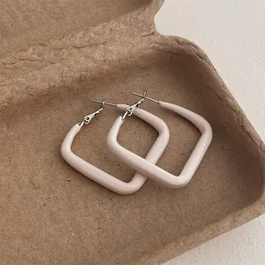 Detailed view of square cream enamel hoop earrings with a matte geometric texture