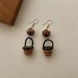 Close-up of handmade wicker basket drop earrings with wooden beads on fabric background