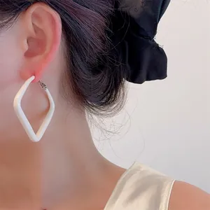 Close-up of a model wearing minimalist white geometric rhombus earrings with matte lacquer finish