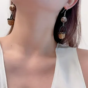 Detailed view of handmade woven basket earrings with wood bead on model neck