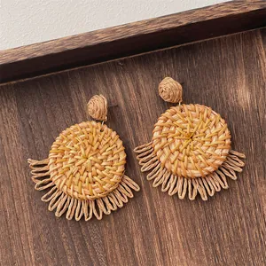 Macro detail of handmade bohemian straw woven earrings with circular fringe on wood