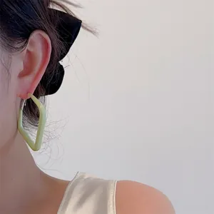 Close-up of light green geometric lacquer earrings worn to show style and scale
