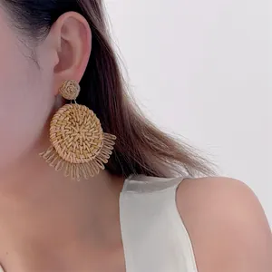Detail of woven raffia earrings with fringe pendants shown on a model for beach style