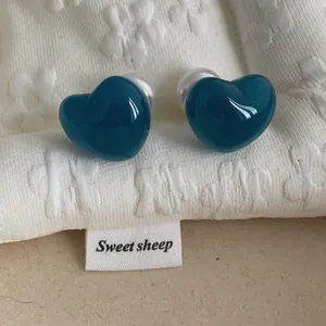 Detailed close-up of dark teal heart-shaped stud earrings with white pearl backings