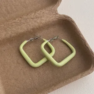 Detail of light green square geometric hoop earrings resting in a kraft gift box
