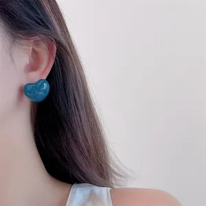 Peacock blue heart stud earrings with glossy finish shown on model ear for style reference