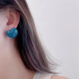 Close-up of a model wearing glossy dark blue heart-shaped stud earrings in a minimalist style